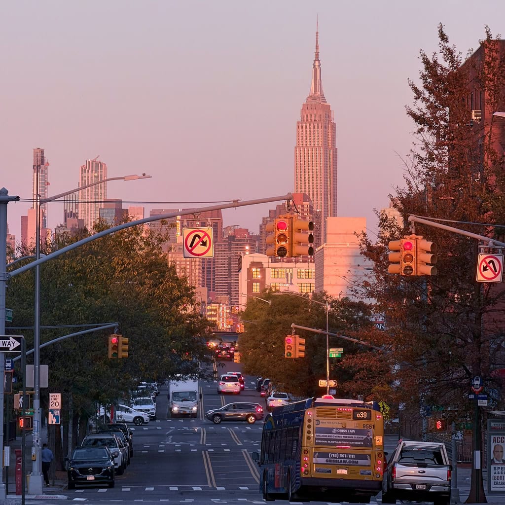 Urban street scene at sunset with the Empire State Building in the distance, cars and traffic lights in the foreground
